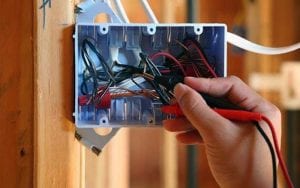 Image of a commercial electrician in Dover NH's hand holding wires and tools troubleshooting a outlet box